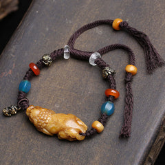 Bone PiXiu Braided Rope Bracelet – Flat lay on dark stone, carved bone Pi Xiu, blue and red agate beads, brown cord