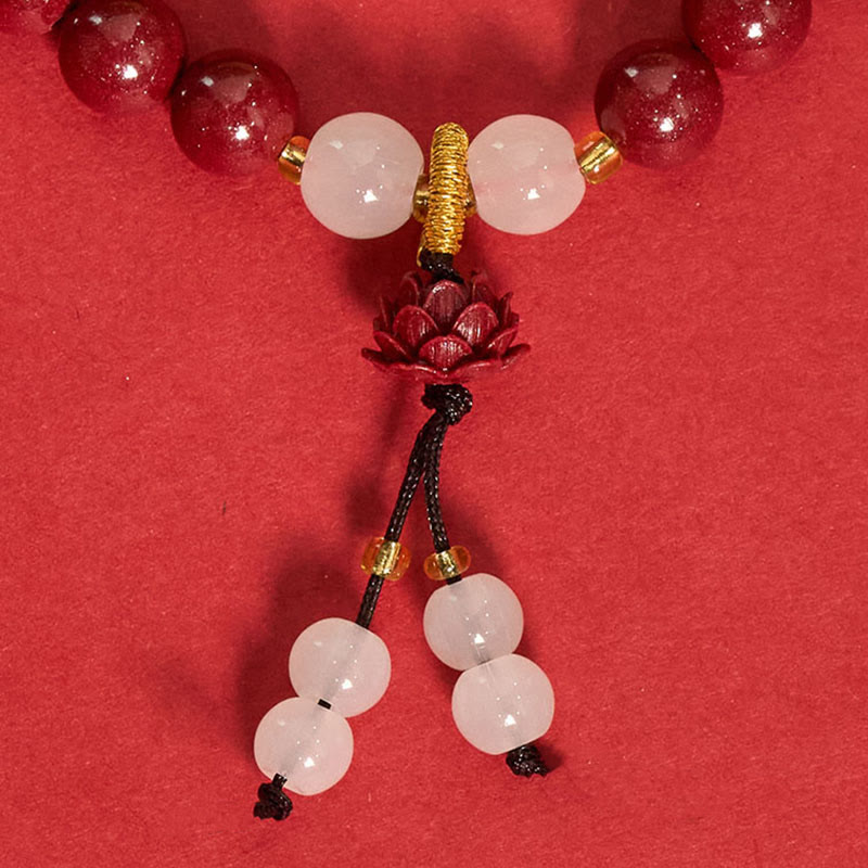 Cinnabar Lotus Enlightenment Bracelet – draped on red surface showing black cord tassels with terminating jade beads, mala bracelet