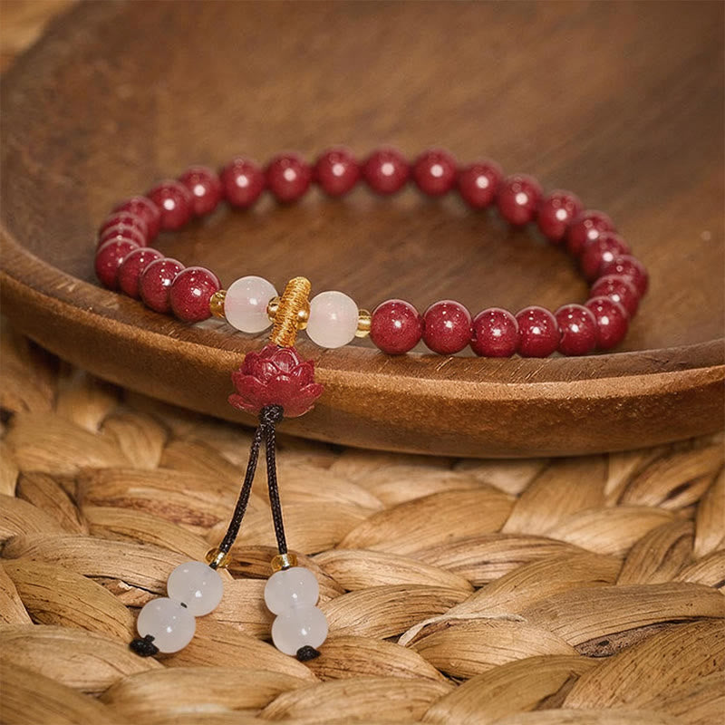 Cinnabar Lotus Enlightenment Bracelet – resting in aged wooden bowl on woven rattan mat, lotus charm and tassel dangle, spiritual jewelry