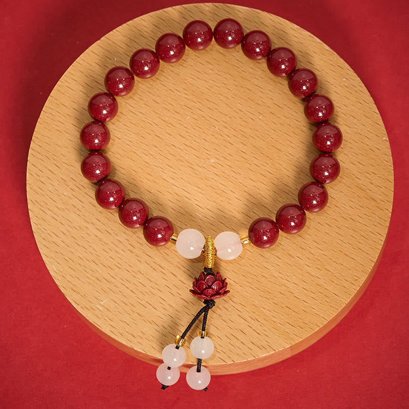 Cinnabar Lotus Enlightenment Bracelet – flat lay on wooden disc with dried botanical accents, full tassel detail, protective jewelry