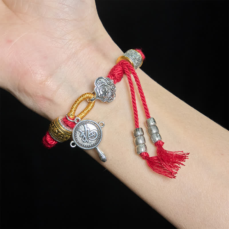 Fu Swastika Rope Bracelet - Close-up thick braided red cord bracelet with gold-tone hardware on beige fabric, woven rope texture detail