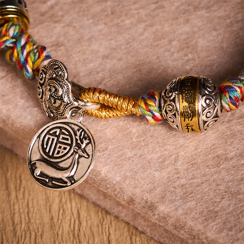 Fu Swastika Rope Bracelet - Green braided cord bracelet with silver gold Tibetan prayer wheel charms on wooden surface, handmade spiritual jewelry