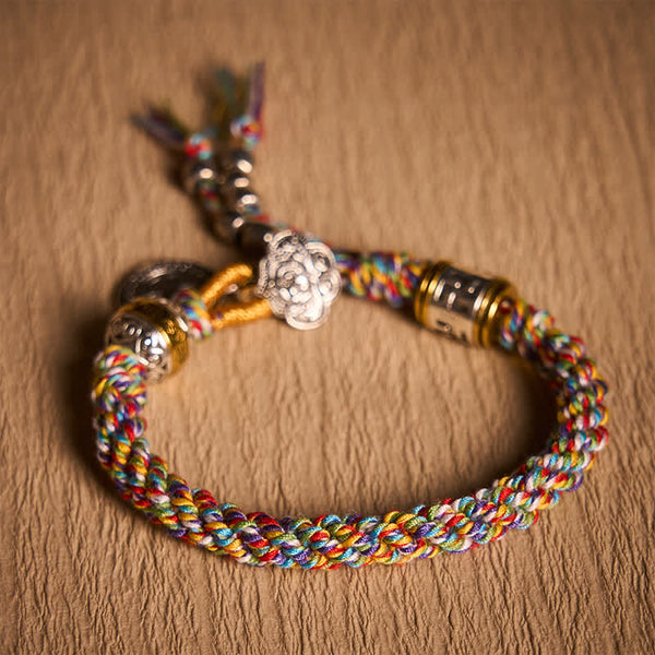 Fu Swastika Rope Bracelet - Close-up rainbow braided cord bracelet with gold bead accents on beige fabric, multicolor woven bracelet detail