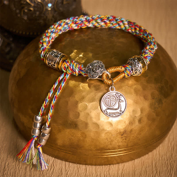 Fu Swastika Rope Bracelet - Tibetan Buddhist braided bracelet with rainbow threads, prayer wheel charms and fortune pendant on wooden surface