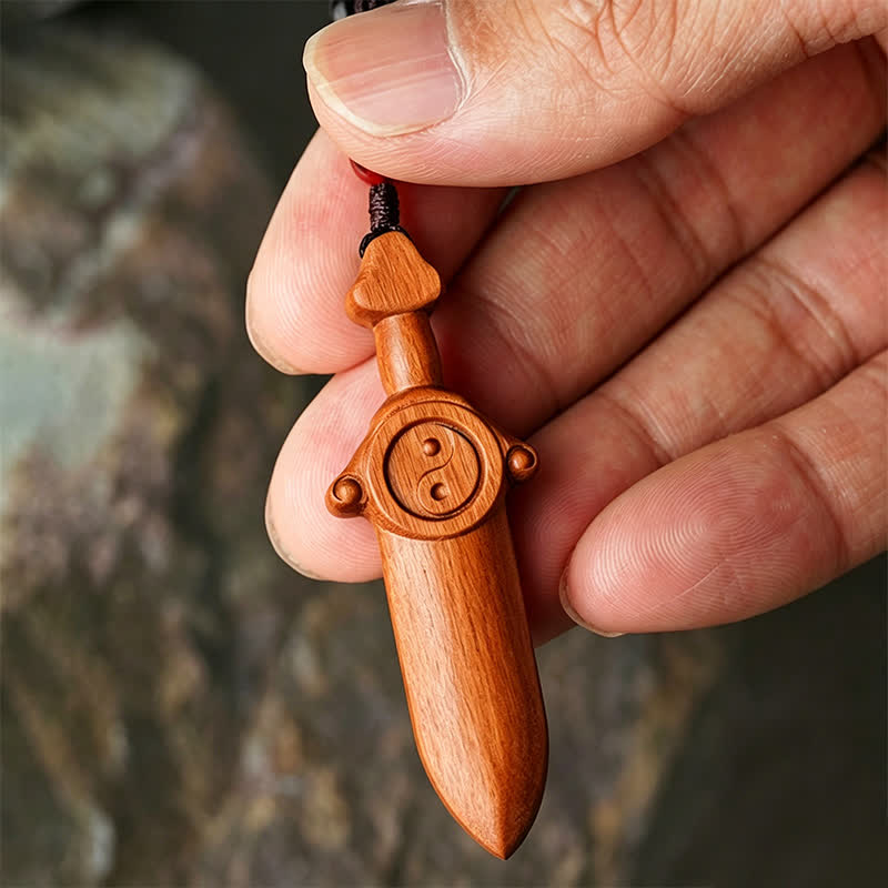 Yin Yang Sword Keychain - Hand-carved wood sword with yin-yang symbol held in hand outdoors, braided cord with red bead, trad
