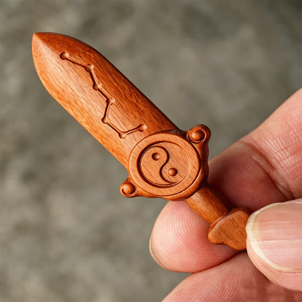Yin Yang Sword Keychain - Hand holding carved wooden sword pendant showing yin-yang guard and Big Dipper blade detail, natura