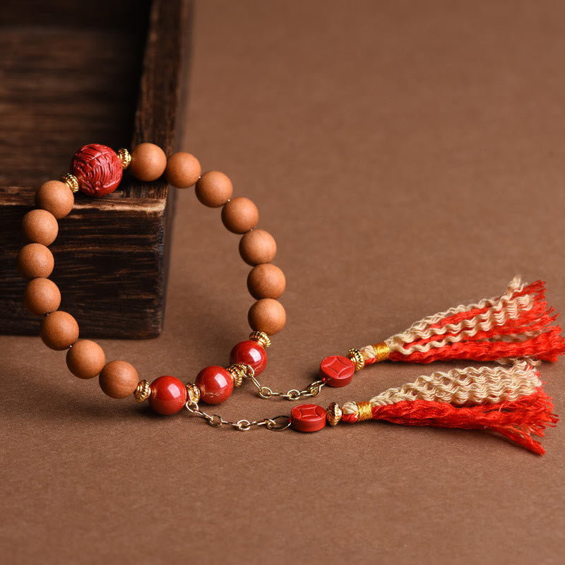 Peach Wood PiXiu Wealth Bracelet – Sandalwood cinnabar bracelet with gold tassel on brown surface, zen jewelry
