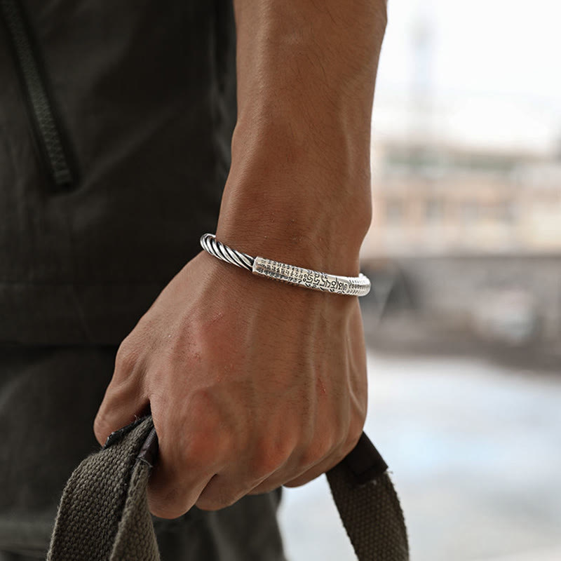 Tibetan Heart Sutra Cuff Bracelet – on wrist gripping bag strap, blurred urban background, men's silver cuff
