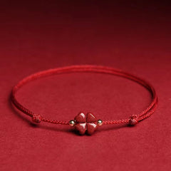 Red cord bracelet with cinnabar four leaf clover carved bead gold-tone spacer beads and adjustable sliding knot closure on red fabric monochromatic background