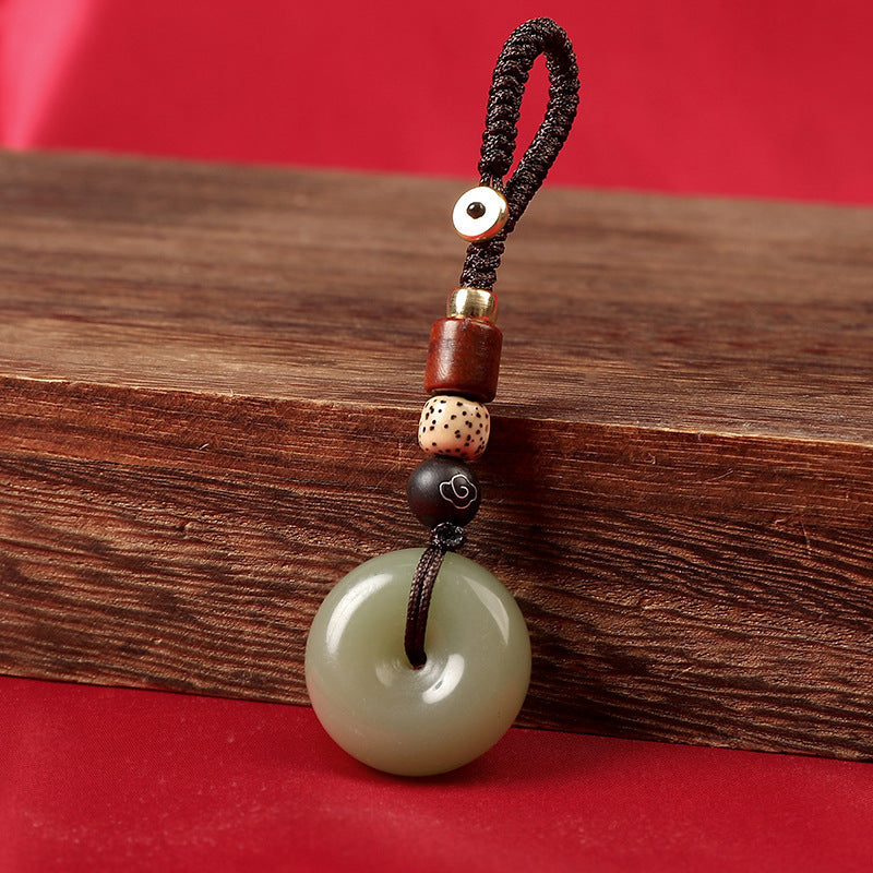 Natural celadon agate ping an kou keychain on wooden block with red backdrop