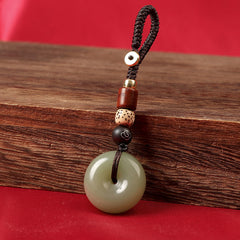 Natural celadon agate ping an kou keychain on wooden block with red backdrop
