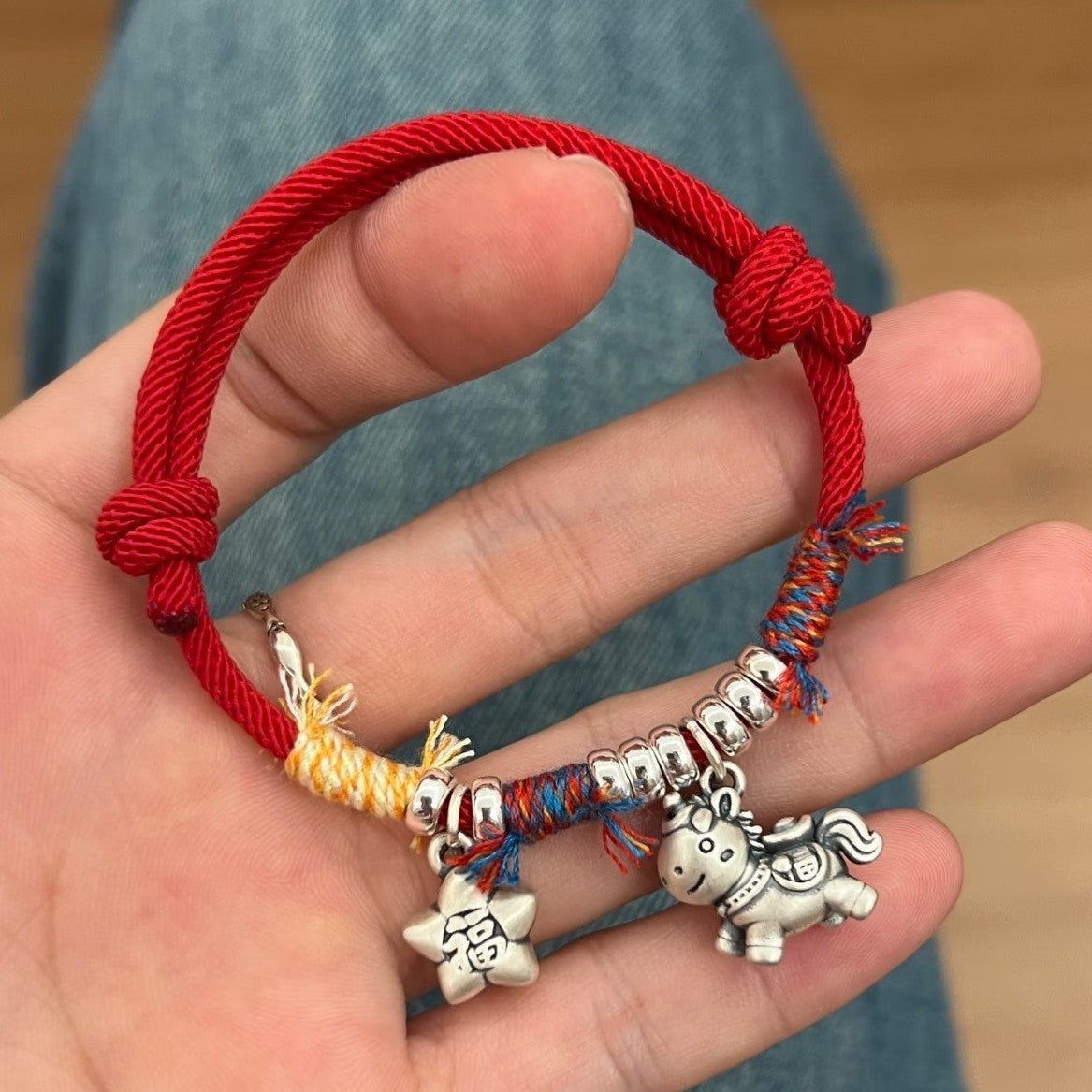 Horse Red String Bracelet – Close-up of silver horse pendant and colorful knots on red cord in hand, fu ma