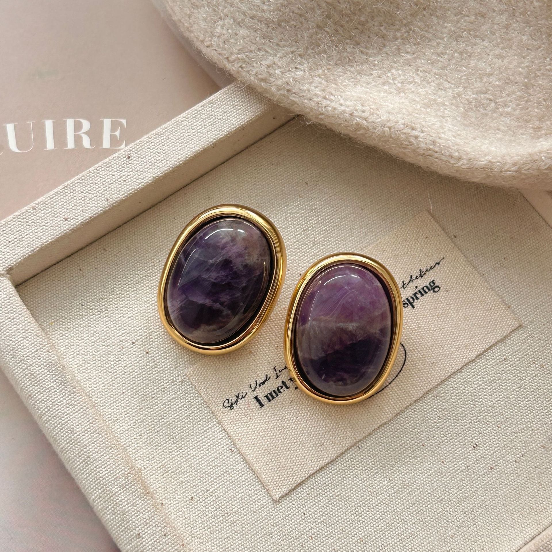 Amethyst Stud Earrings – purple amethyst oval studs in gold frames on beige canvas jewelry tray with knit fabric, bohemian earrings