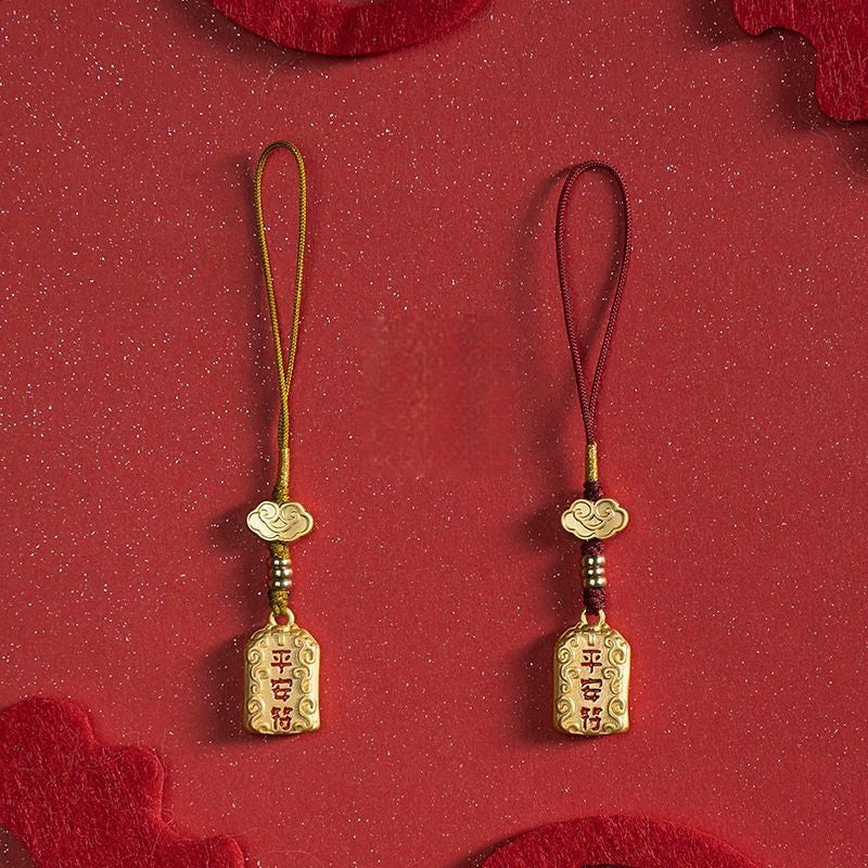 Two brass peace charms side by side with gold and red cords on red background