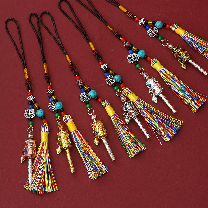 Tibetan Prayer Wheel Keychain – gold-tone prayer wheel pendant with colorful silk tassel, turquoise beads and full braided cord, red background, front vertical view