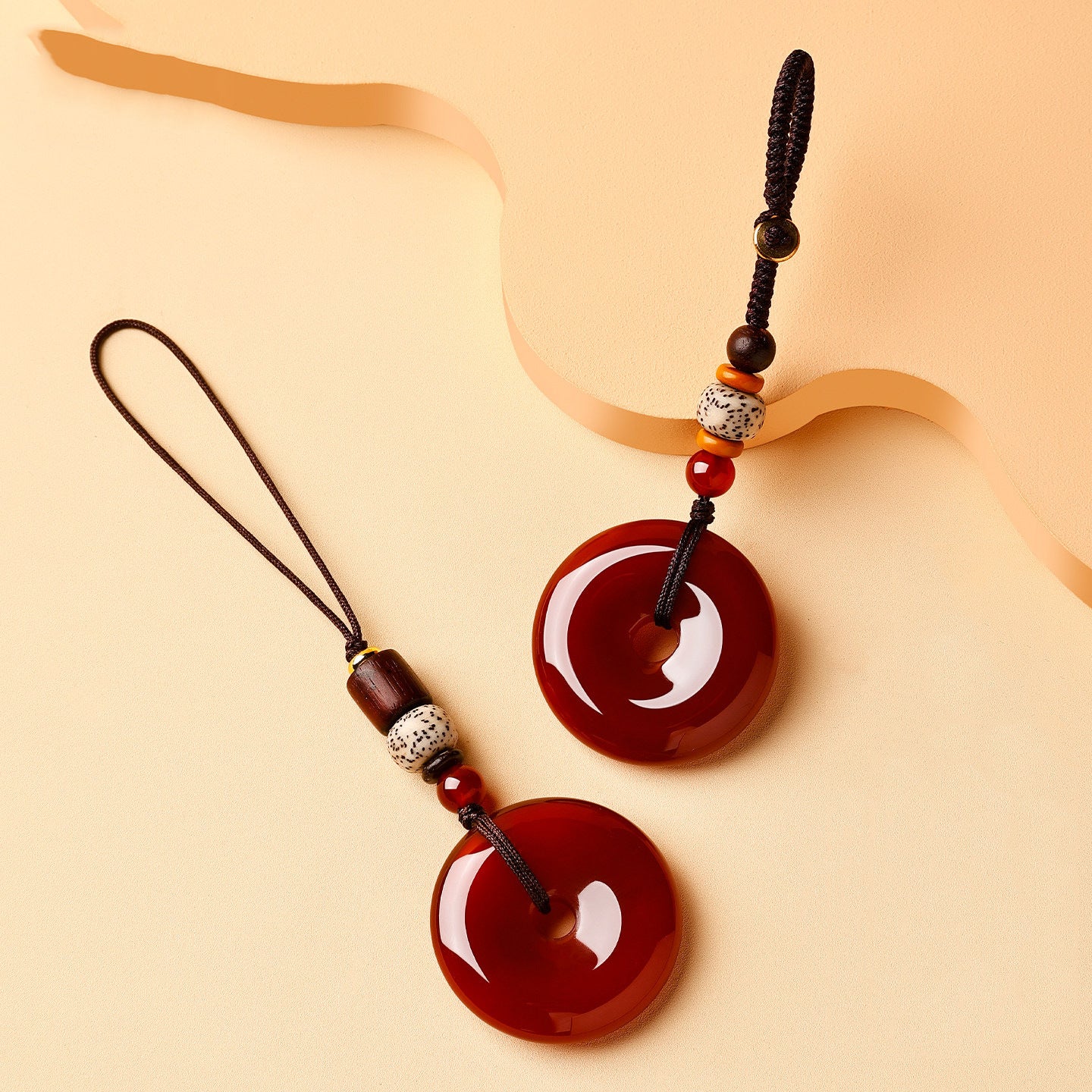 Jade Keychain Pendant – Two red-brown jade donuts thick and thin cord style on beige with wave decor, comparison