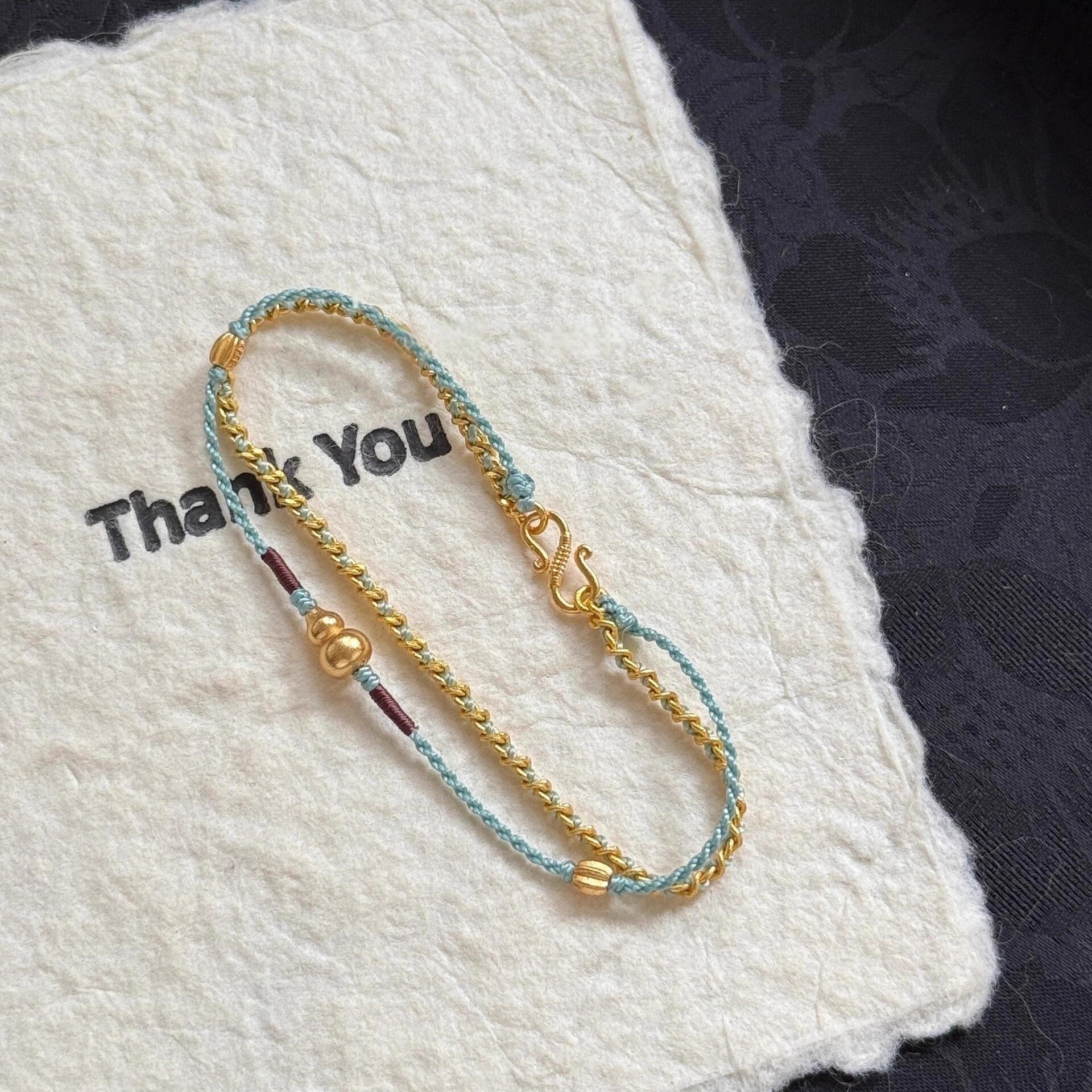 Double-Layer Gourd Bracelet – Angled view of gold chain and blue cord with gourd pendant on fabric, luck jewelry