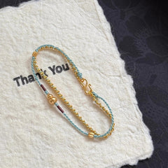 Double-Layer Gourd Bracelet – Angled view of gold chain and blue cord with gourd pendant on fabric, luck jewelry