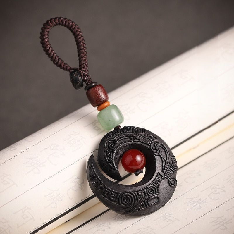 Feng Shui ebony wood protection keychain spiral moon design with red bead on gray textured background