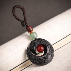 Feng Shui ebony wood protection keychain spiral moon design with red bead on gray textured background