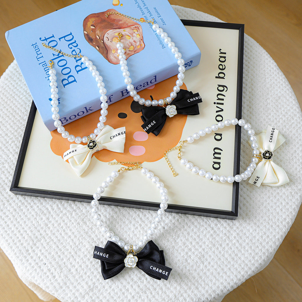 Luxury Crystal Pet Necklace – four pearl collars with black and cream satin bows, camellia charms, lifestyle flat lay
