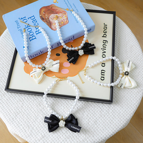 Luxury Crystal Pet Necklace – four pearl collars with black and cream satin bows, camellia charms, lifestyle flat lay