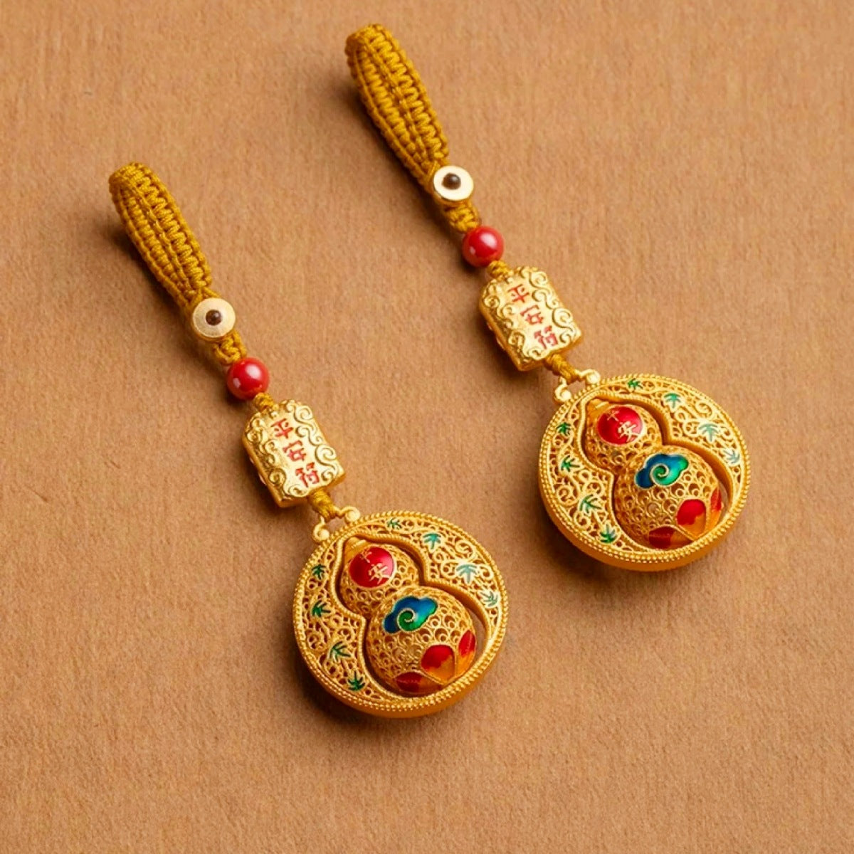 Gold rotating calabash disc keychain with peace talisman, red cord on white wood
