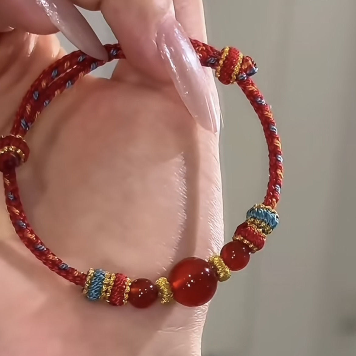 Dunhuang Agate Bracelet – red agate bracelet on feminine wrist with manicured nails held gently against light grey background, handmade jewelry