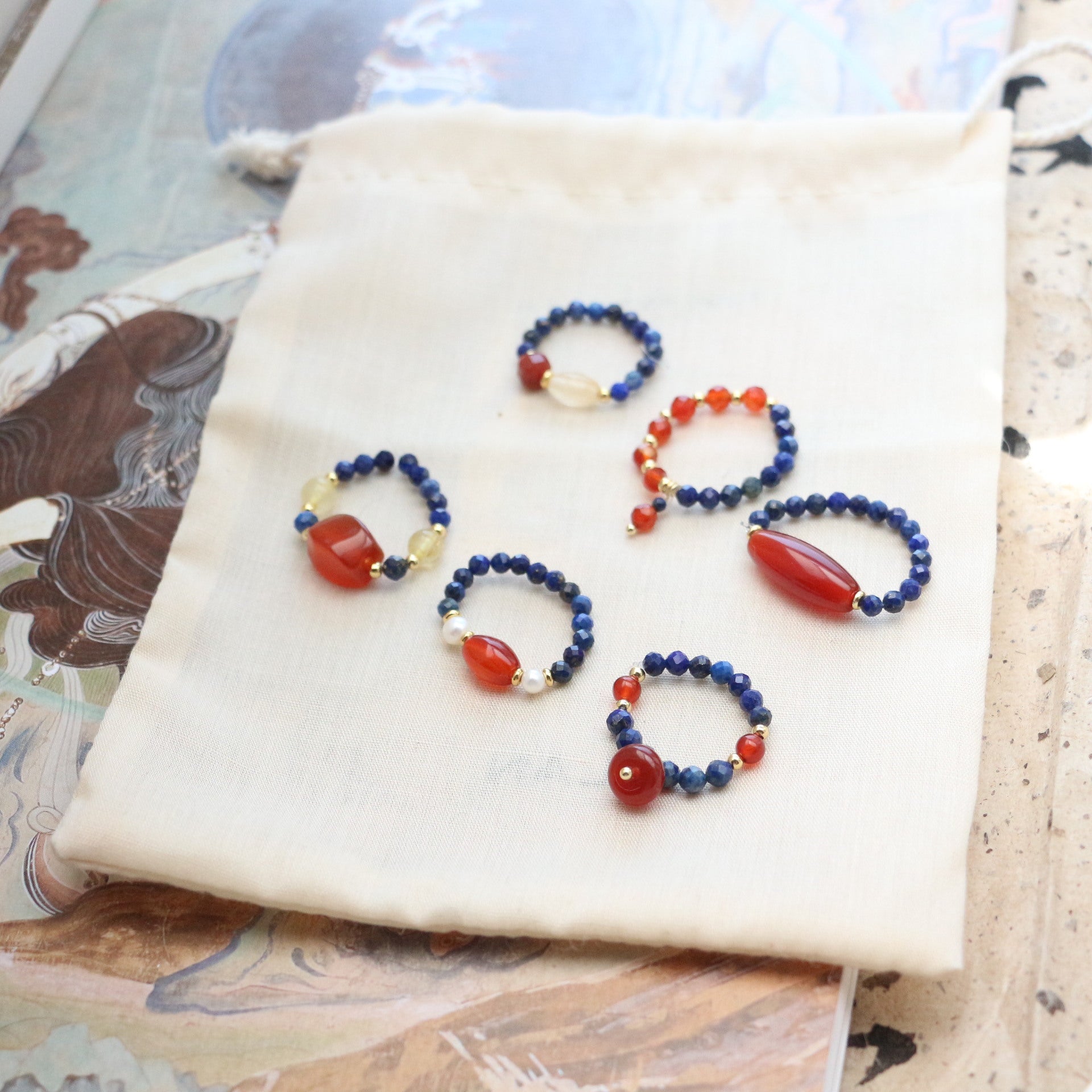 Lapis Lazuli Agate Ring Set – six assorted rings displayed on cream pouch, mix of blue lapis and red agate designs, crystal collection