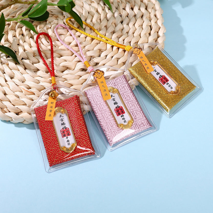 Three colorful heavenly blessing amulets in red, pink and gold on woven mat Imagen principal del producto