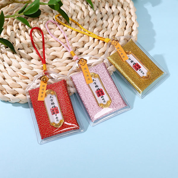 Three colorful heavenly blessing amulets in red, pink and gold on woven mat