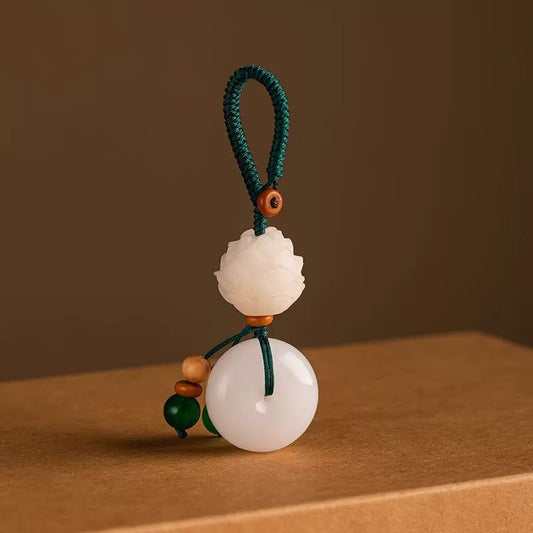 Chalcedony Lotus Keychain – white jade-like lotus peace buckle on brown surface with green cord, harmony charm