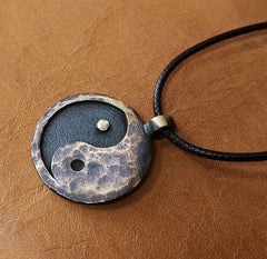 Yin Yang Pendant – hammered bronze yin-yang disc lying on tan leather surface, textured detail view