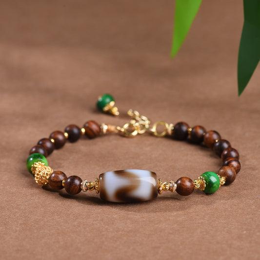 Dzi Rosewood Bracelet – Bracelet with dzi bead and green stones on brown surface with leaves, protection jewelry