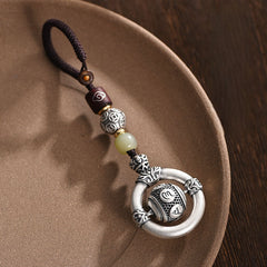 Mantra Keychain – ornate silver amulet resting on ceramic dish, jade bead detail, carved mantra