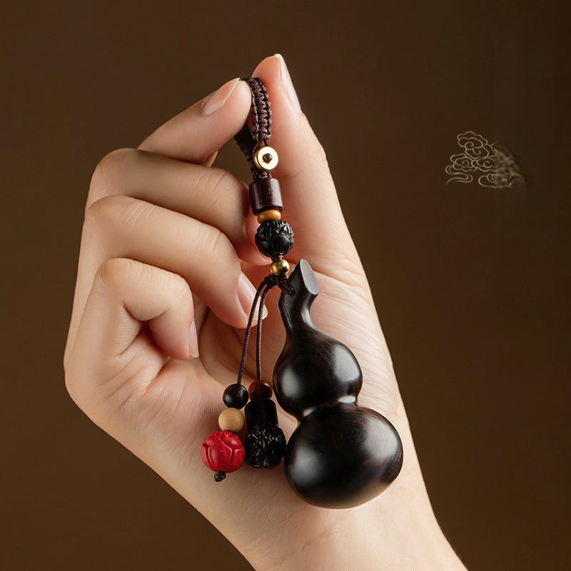 Sandalwood Gourd Keychain – hand holding dark gourd charm against brown background with cloud motif