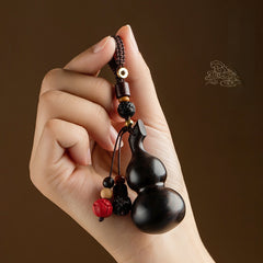 Sandalwood Gourd Keychain – hand holding dark gourd charm against brown background with cloud motif