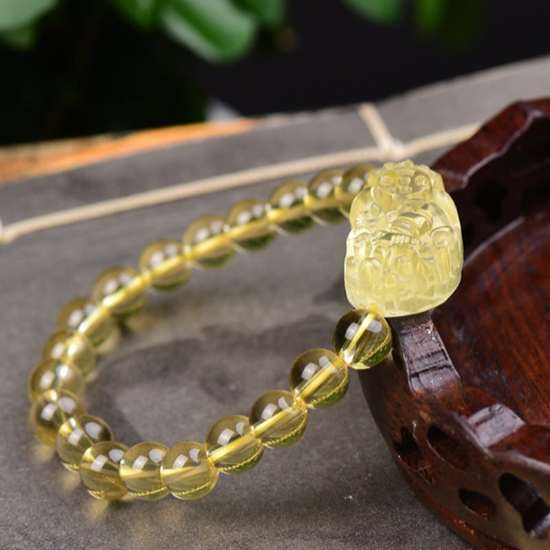 Citrine PiXiu Wealth Bracelet – side angle showing detailed PiXiu carving next to wooden decor, yellow crystal beads, good luck charm
