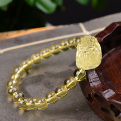 Citrine PiXiu Wealth Bracelet – side angle showing detailed PiXiu carving next to wooden decor, yellow crystal beads, good luck charm
