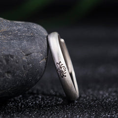Lotus Enlightenment Ring - oxidized lotus band leaning against dark river stone, artisan