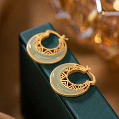 Crescent Moon Jade Drop Earrings – Gold double-ring hoop earrings with white jade crescent inlay and geometric cutouts, cream fabric jewelry box, low macro