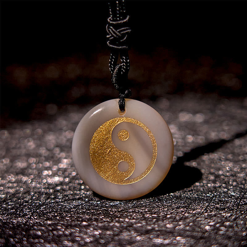 Yin Yang Crystal Necklace – White jade round pendant with gold yin-yang symbol inlay, pale beige polished stone on black cord