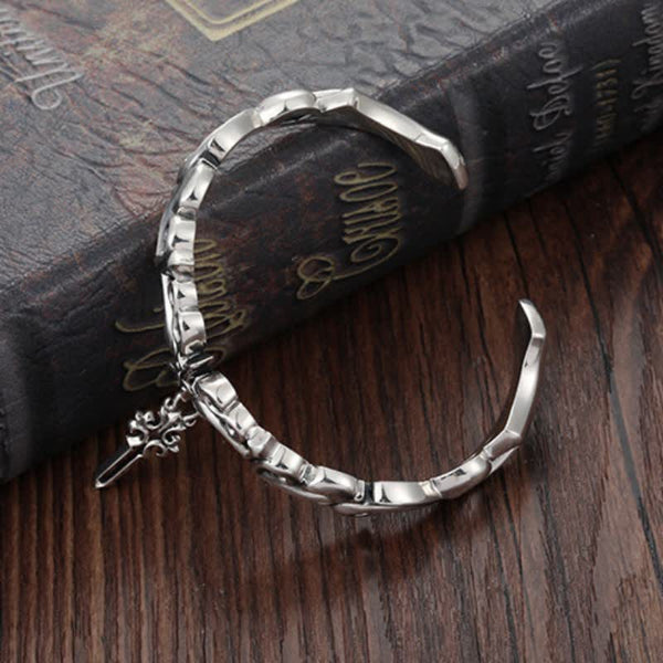 Men's twisted rope silver bracelet with gothic geometric links and decorative sword charm pendant on vintage book with Shakespeare text dark wood background