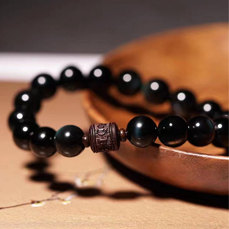 Gold Sheen & Rainbow Obsidian Fu Bracelet – worn on wrist resting on book, lifestyle jewelry shot