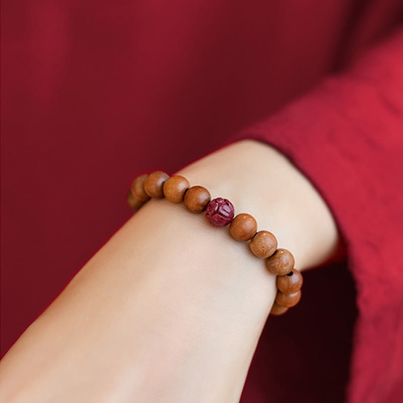 Peach Wood & Cinnabar Lotus Bracelet on wrist with red sleeve, elastic wood bead stretch band, carved lotus focal, zen living
