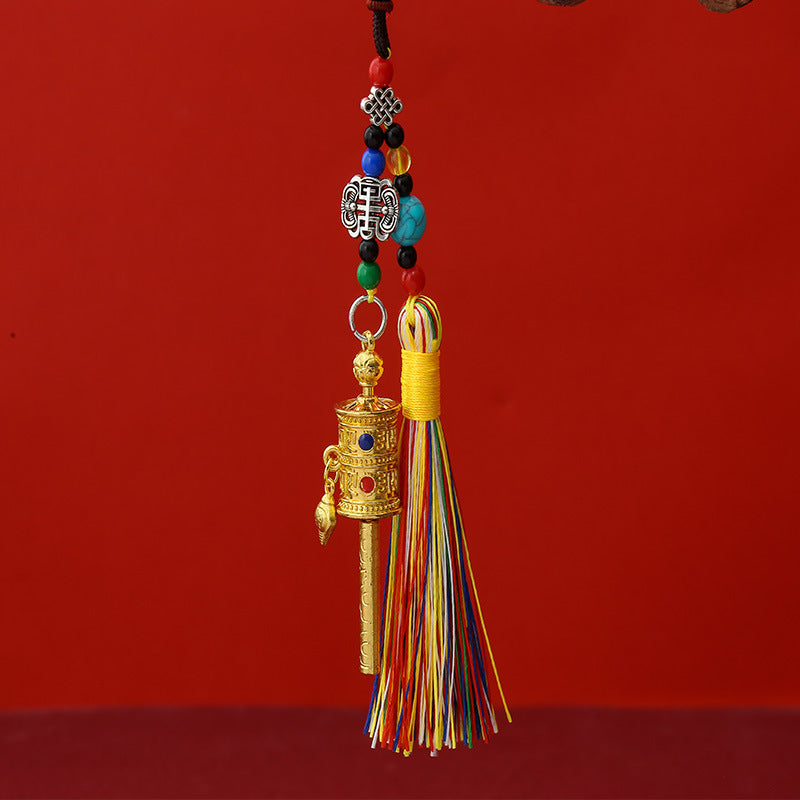 Tibetan Prayer Wheel Keychain – gold-tone prayer wheel pendant with colorful silk tassel, turquoise beads and auspicious knot charm, red background, front vertical view