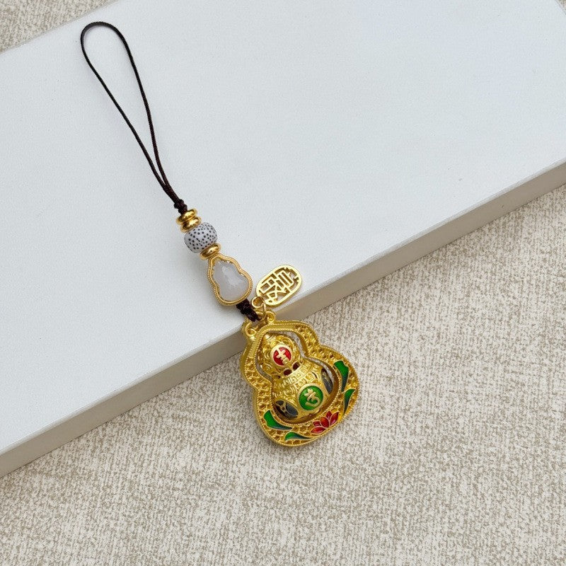 Gold rotating calabash keychain with peace talisman and golden cord, white wood backdrop