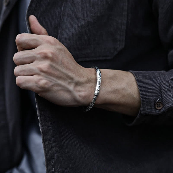 Viking twisted braided bracelet with engraved runic characters central nameplate rope-textured band edges worn on male wrist with dark jacket showing heritage design