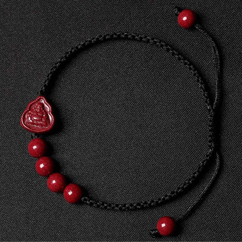 Cinnabar Laughing Buddha Guan Yin Bracelet – black cord with cinnabar beads and Buddha teardrop pendant, dark textured flat lay