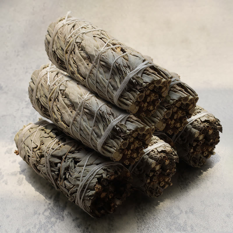 Four white sage smudge sticks bundled with twine on gray stone surface